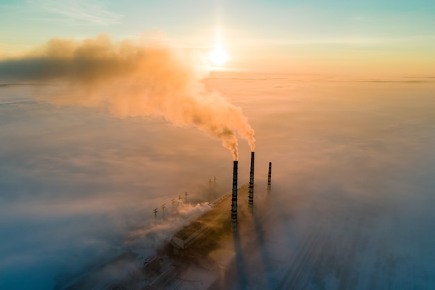 Widok z lotu ptaka wysokich rur elektrowni węglowej z czarnym dymem poruszającym się w górę zanieczyszczającej atmosfery o zachodzie słońca.