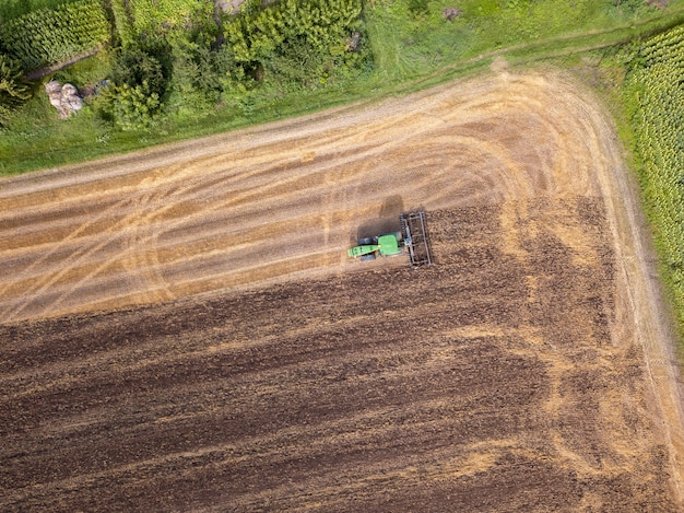 Widok z lotu ptaka z drona pola po zbiorach. Ciągnik orze pole, przygotowując glebę do prac rolniczych.