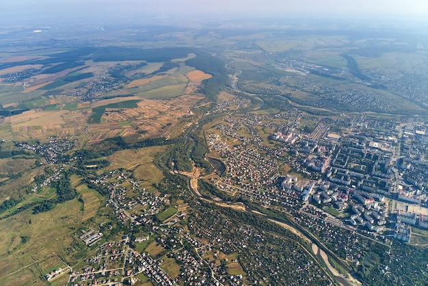 Widok z lotu ptaka z okna samolotu na dużej wysokości odległego miasta pokrytego warstwą cienkiego mglistego smogu i odległych chmur wieczorem