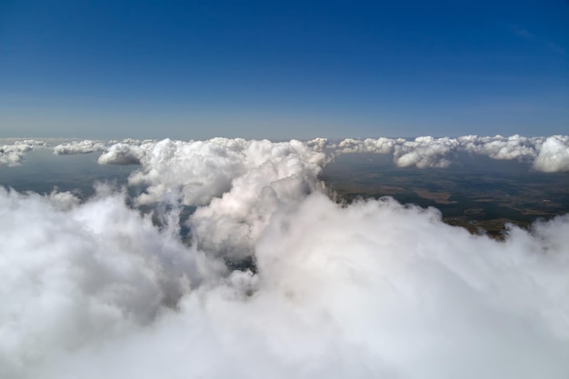Widok z lotu ptaka z okna samolotu na dużej wysokości ziemi pokrytej białymi podpuchniętymi chmurami cumulus.
