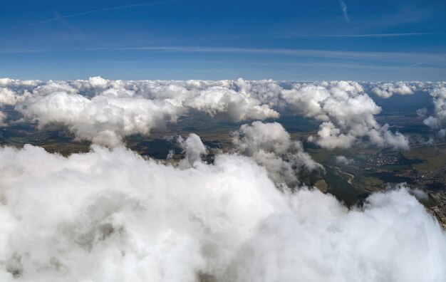 Widok z lotu ptaka z okna samolotu na dużej wysokości ziemi pokrytej białymi, puszystymi chmurami cumulus