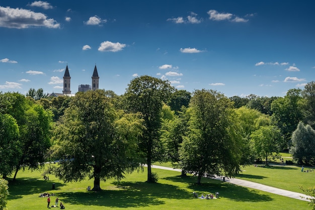 Widok z łuku ogrodu angielskiego w Monachium. Widok z lotu ptaka na panoramę Monachium z "Englischer Garten" i rzeką "Eisbach" z przodu. Ludzie opalający się w Ogrodzie Angielskim w Bawarii