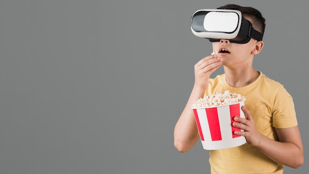 Zdjęcie widok z przodu chłopiec ogląda film na wirtualnej rzeczywistości słuchawki i jedzenie popcornu