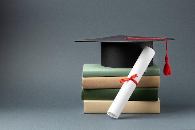 Zdjęcie widok z przodu czapki dyplomowej, dyplomu i ułożonych w stos książek z miejscem na kopię na dzień edukacji