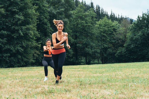 Widok z przodu dwóch kobiet wykonujących ćwiczenia siłowe z gumką, dużo wysiłku w środku lasu
