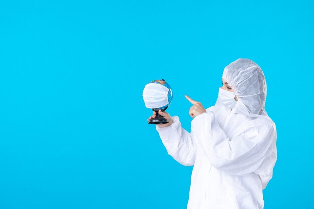 widok z przodu lekarka w kombinezonie ochronnym i masce trzymającej zamaskowany glob na niebieskim tle kolor wirus covid nauka pandemia zdrowie