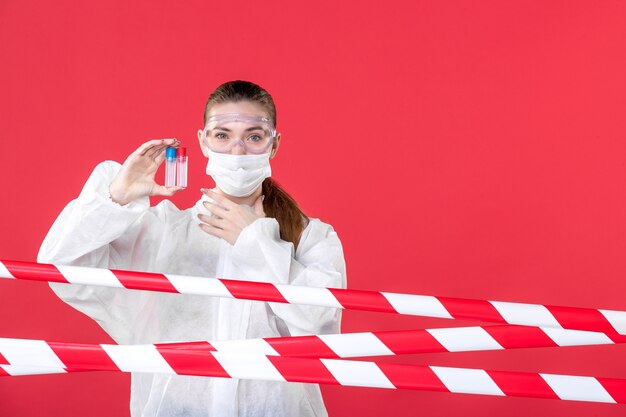 widok z przodu lekarka w kombinezonie ochronnym trzymająca kolby na czerwonym tle pielęgniarka covid- zdrowie leczenie tkanki emocje wirus maska szpital