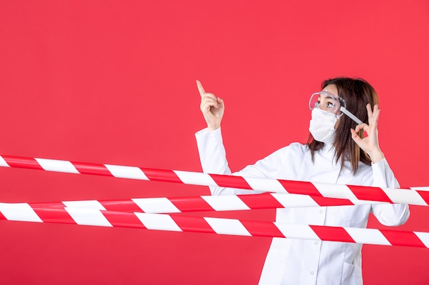 widok z przodu lekarka w mundurze medycznym i masce na czerwonym tle zapieczętowana przestępczość covid - izolacja linii zdrowia wirusa szpitalnego