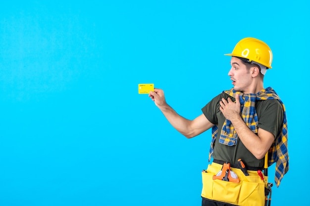 widok z przodu męski budowniczy w żółtym kasku trzymający kartę bankową na niebieskim tle pieniądze architektura konstruktor budowlany płaski kolor pracownik
