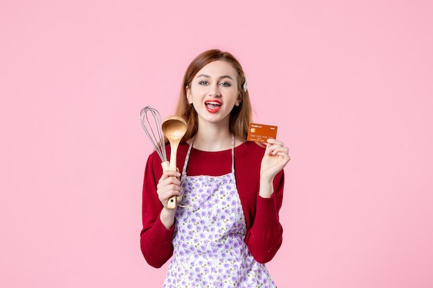 widok z przodu młoda gospodyni trzymająca trzepaczkę i kartę bankową na różowym tle kuchnia ciasto ciasto kobieta zakupy pieniądze kuchnia jedzenie kolor gotowanie