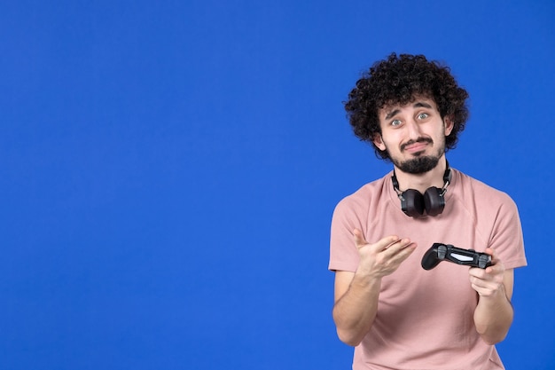 widok z przodu młody człowiek grający w grę wideo z czarnym gamepadem na niebieskim tle nastoletnia młodzież wygrywająca sofa dorosła wirtualna radość piłka nożna