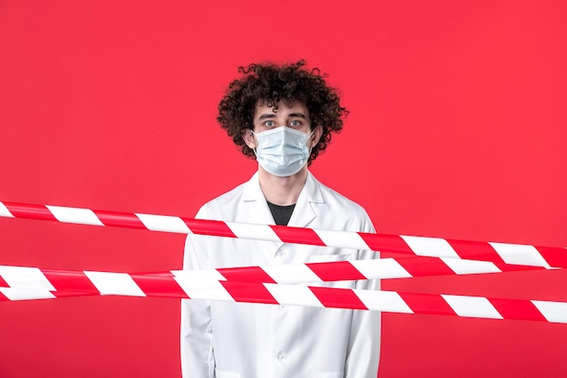 Zdjęcie widok z przodu młody mężczyzna lekarz w mundurze medycznym i masce na czerwonym tle izolacja szpital lek covid niebezpieczeństwo ostrzeżenie kwarantanna zdrowotna
