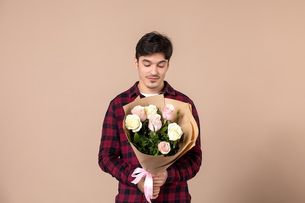 Widok z przodu młody mężczyzna trzymający piękne kwiaty na brązowej ścianie