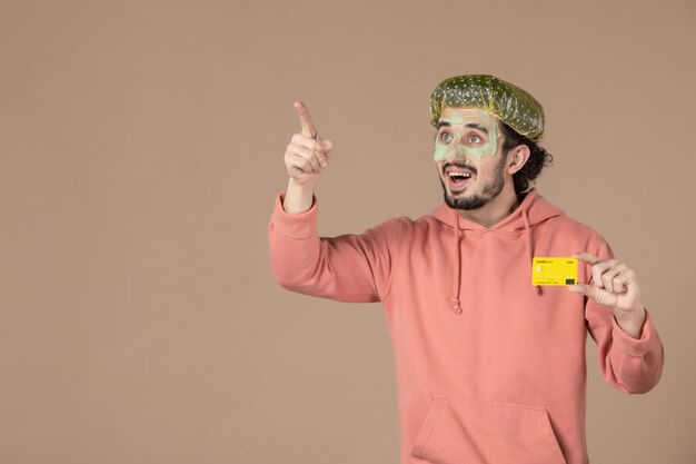 widok z przodu młody mężczyzna trzymający żółtą kartę kredytową na brązowym tle spa pielęgnacja ciała terapia pieniędzmi salon pielęgnacji skóry skóra twarzy