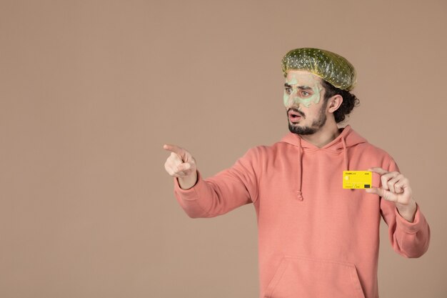 widok z przodu młody mężczyzna trzymający żółtą kartę kredytową na brązowym tle spa skóra pielęgnacja ciała terapia pieniężna salon pielęgnacji skóry kolor twarzy