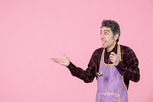 widok z przodu młody mężczyzna w pelerynie trzymający łyżkę do zupy i wchodzący w interakcję z kimś na różowym tle gotować kuchnia jedzenie horyzontalny zawód mąż pracownik