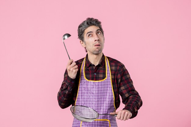 widok z przodu młody mężczyzna w pelerynie z sitkiem i łyżką na różowym tle kuchnia pracownik kuchenny mundur jedzenie mąż zupa zawód kucharz
