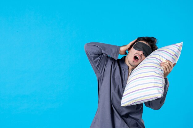 widok z przodu młody mężczyzna w piżamie próbujący zasnąć na poduszce na niebieskim tle człowiek obudzić łóżko odpoczynek kolor noc późny koszmar sen