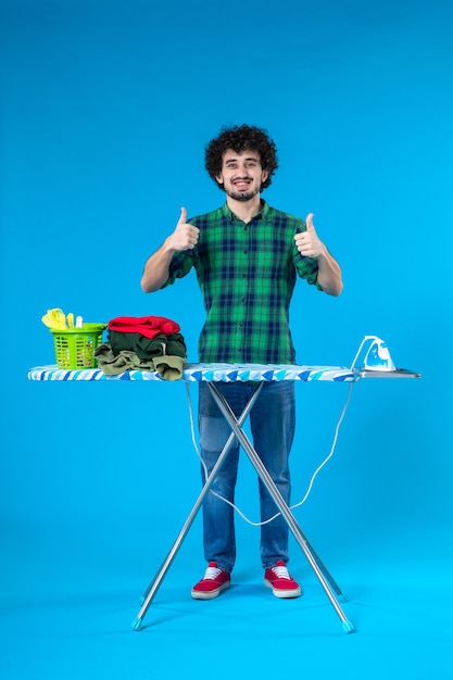widok z przodu młody mężczyzna z deską do prasowania uśmiechający się na niebieskim tle dom ubrania czyste pralka ludzkie żelazo prace domowe