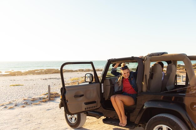 Widok z przodu odległej kobiety rasy kaukaskiej wewnątrz otwartego samochodu z otwartymi drzwiami, uśmiecha się. Weekendowe wakacje na plaży, styl życia i wypoczynek.
