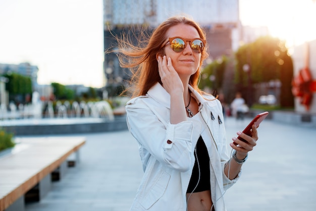 Widok Z Przodu Portret Nowoczesnej Mody Szczęśliwa Kobieta Hipster Chodzenia I Korzystania Z Inteligentnego Telefonu Na Ulicy Miasta W Okularach Przeciwsłonecznych W Letnim Słońcu. Internet, Usługa Online, Telefon, Dziewczyna, Kobieta