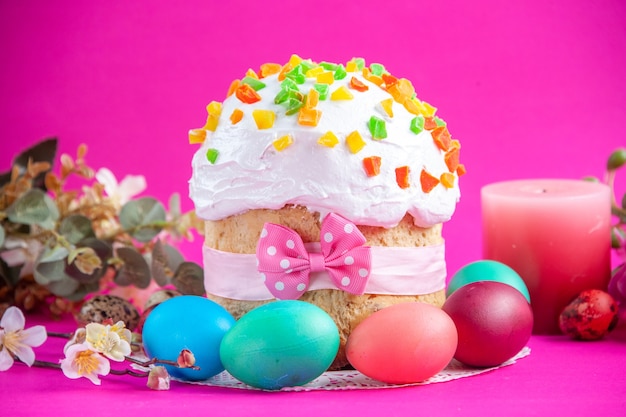 widok z przodu pyszne kremowe ciasto z kolorowymi jajkami i świeczką na różowym tle cukier kolorowy ozdobny novruz słodki wiosenny deser wakacyjny