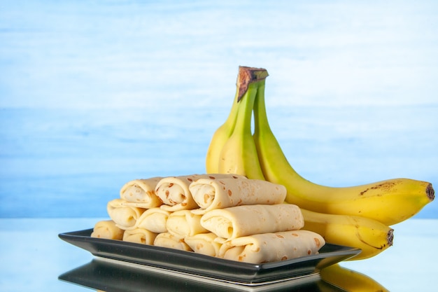 widok z przodu pyszne rolowane naleśniki z bananami na jasnoniebieskim tle deser cukier rano śniadanie kolor mleko słodkie ciasto