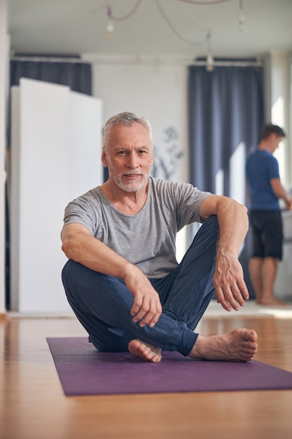 Widok z przodu siwego mężczyzny siedzącego na macie do jogi w studiu fitness