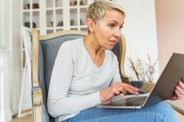 Widok z przodu starszej, krótkowłosej freelancerki rasy kaukaskiej, patrzącej szeroko otwartymi oczami na ekran laptopa