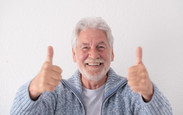 Widok z przodu uśmiechniętego szczęśliwego starszego dziadka patrzącego na kamerę z kciukami do góry wyrażającymi pozytywne myśli na przyszłość