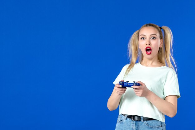 widok z przodu zaskoczona młoda kobieta grająca w grę wideo z gamepadem na niebieskim tle gracz wygrywający dorosłą sofę internet młodzież wirtualne wideo online radosne