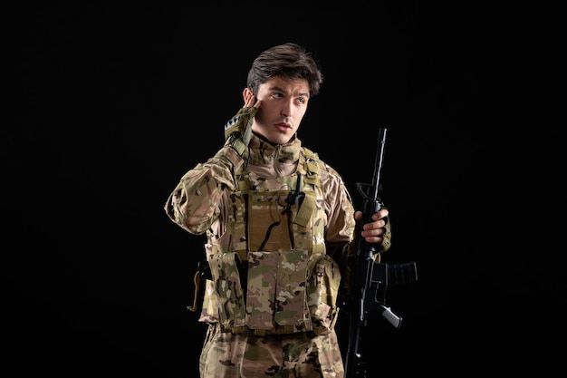 Widok z przodu żołnierz wojskowy w mundurze z karabinem na czarnej ścianie