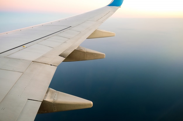 Widok z samolotu na białym skrzydle samolotu lecącego nad krajobrazem oceanu w słoneczny poranek. Koncepcja podróży i transportu lotniczego.