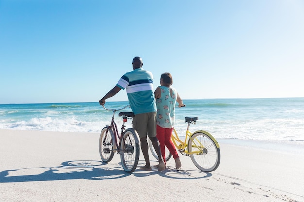 Widok z tyłu Afroamerykanów starszych para na kółkach rowery na plaży z miejsca na kopię na niebieskim niebie