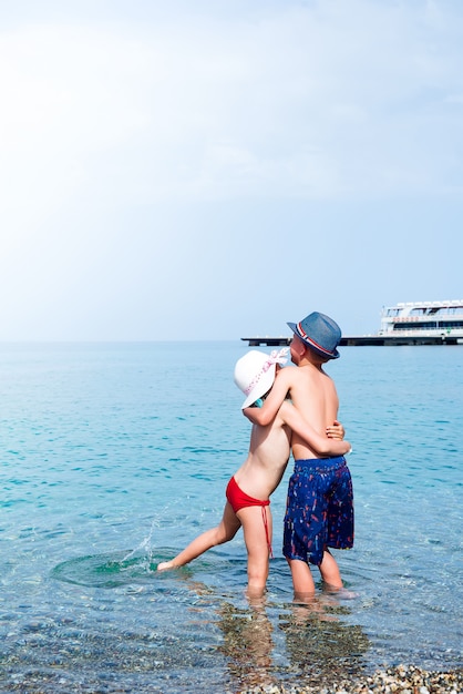 Widok Z Tyłu Babygirl I Babyboy Całuje Się Na Plaży W Słomianych Kapeluszach Nad Morzem.