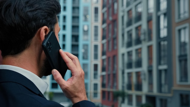 Widok z tyłu biznesmen rozmawia przez telefon komórkowy na zewnątrz na ulicy miasta, korzystając z bezprzewodowego połączenia komórkowego