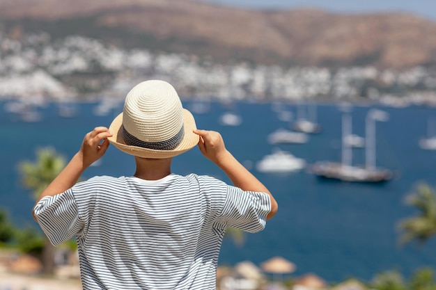 Widok z tyłu chłopca na sobie pasiastą koszulkę i letni kapelusz, obserwując morze z góry Koncepcja wakacji letnich