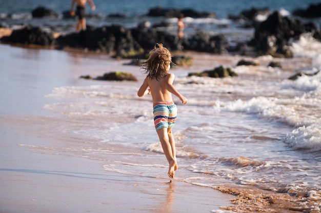 Widok z tyłu chłopca skaczącego i biegającego po plaży?