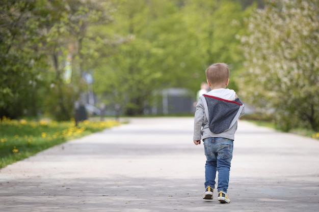 Widok z tyłu chłopca spacerującego samotnie parkową drogą w okresie wiosennym Drzewa w rozkwicie