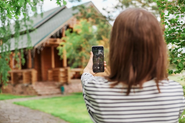 Widok z tyłu ciemnowłosej kobiety robiącej zdjęcia telefonem komórkowym w pasiastej swobodnej koszuli trzymającej smartfon w rękach transmitującej transmisję na żywo