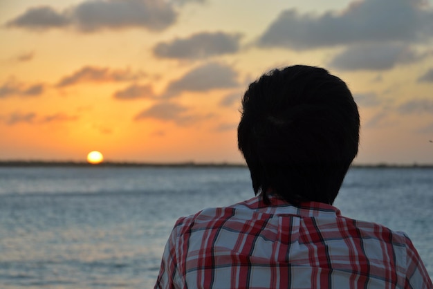 Widok z tyłu człowieka patrzącego na morze na tle zachodu słońca