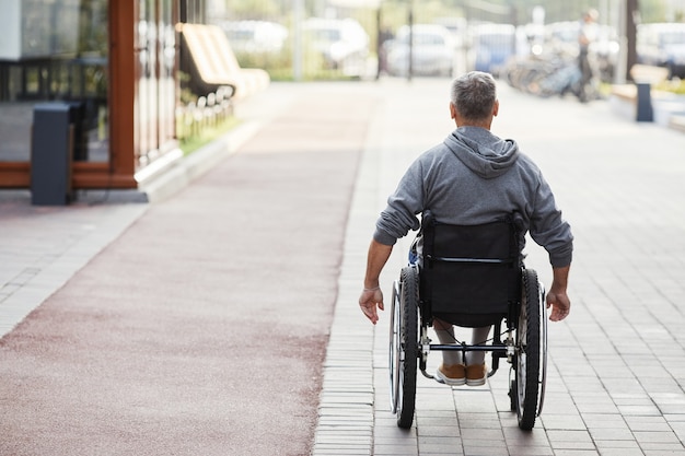 Widok Z Tyłu Dojrzałego Mężczyzny Z Niepełnosprawnością Jadącego Na Wózku Inwalidzkim Wzdłuż Ulicy