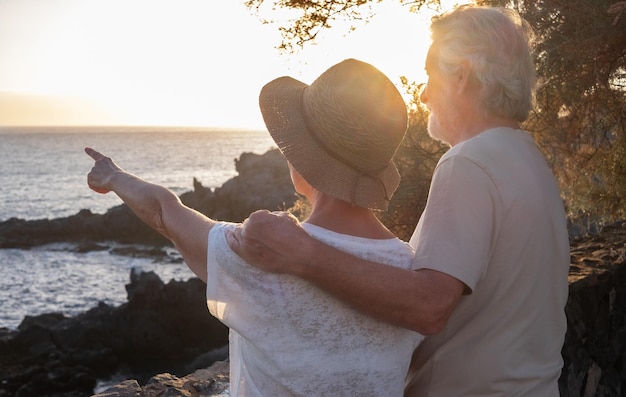 Widok z tyłu dwóch szczęśliwych i romantycznych seniorów lub emerytów w objęciach nad morzem o zachodzie słońca, patrząc na horyzont staruszka na zewnątrz ciesząc się wakacjami razem