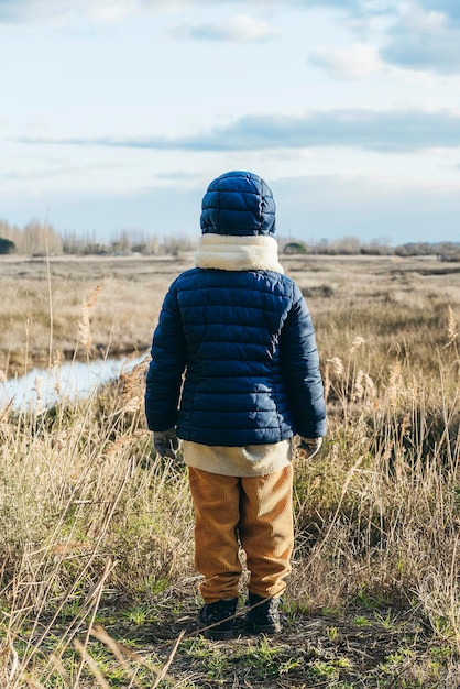 Widok z tyłu dziecka ubranego w zimowe ubrania stojącego przed dzikim krajobrazem Koncepcja Wanderlust w dzikich miejscach Koncepcja przyszłości dla nowych pokoleń i ochrony przyrody Pionowo