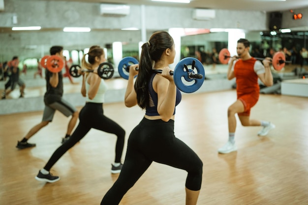 Widok z tyłu grupy sportowej wykonującej przysiady ze sztangą