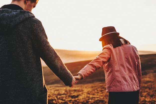 Widok z tyłu kaukaski para trzymająca się za ręce i podróżująca, podczas gdy dziewczyna prowadzi swojego chłopaka przed zachodem słońca w czasie wakacji.