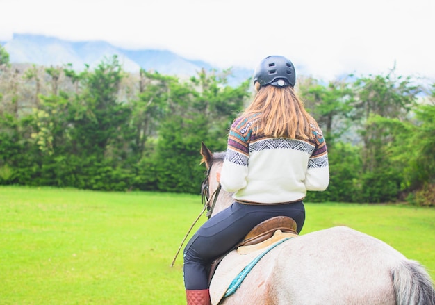 Widok z tyłu kaukaskiej kobiety w andyjskim swetrze i na koniu na łące