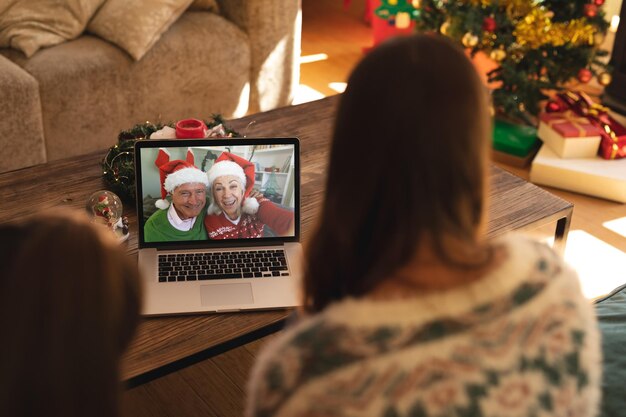 Zdjęcie widok z tyłu kobiety i syna prowadzących rozmowę wideo z parą seniorów w kapeluszach mikołaja uśmiechających się na laptopie w