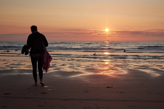 Widok z tyłu kobiety na plaży podziwiającej malowniczy zachód słońca