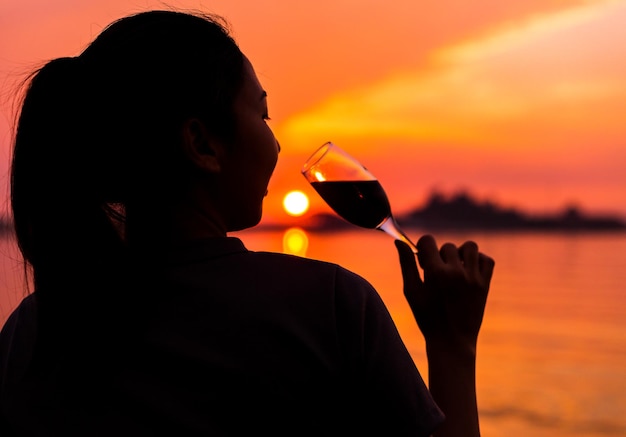 Zdjęcie widok z tyłu kobiety pijącej napoje alkoholowe nad morzem podczas zachodu słońca